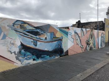 Graffiti on wall by footpath against sky