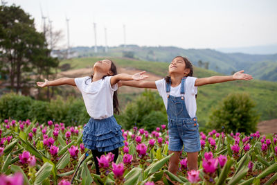 Sisters with arms outstretched standing amidst flowering plants at farm