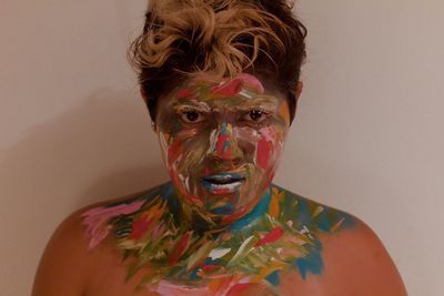 Portrait of topless young woman with colorful paint on face against wall