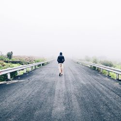 Rear view full length of man walking on road against sky during foggy weather