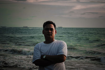 Portrait of young man standing at beach against sky