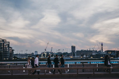 People on bridge over river in city against sky