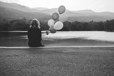 Rear view of woman with balloons sitting by lake