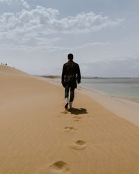 Rear view of man walking on sand dune by beach