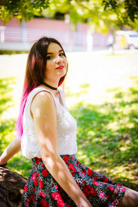 Smiling young woman sitting on tree trunk at park