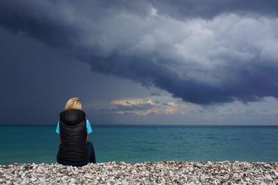 Rear view of woman standing at beach against sky