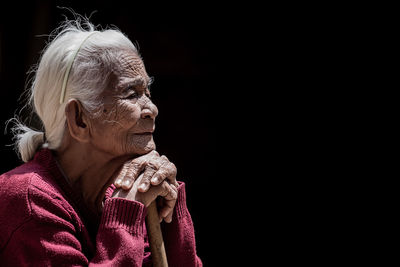 Senior woman leaning on stick against black background