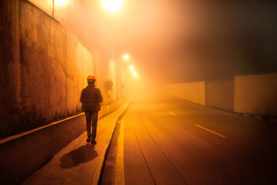 Rear view of man walking on footpath at night