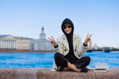 Caucasian happy girl sits on granite curb city with book. in a white coat