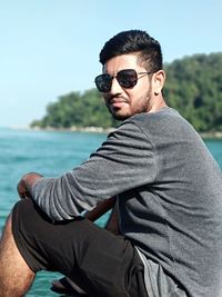 Portrait of young man wearing sunglasses while sitting at sea shore