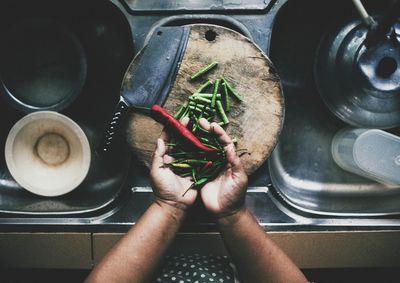 Hand holding chili and green beans over sink