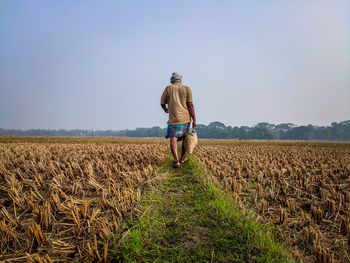 A farmer walks away on a field road with a bag of food on a winter's morning.