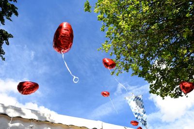 Low angle view of red helium balloons flying against sky