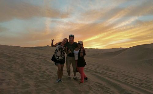 Friends standing on snowy field against sky during sunset