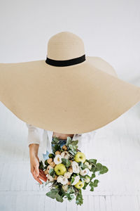 Top view of woman in big straw hat holding bouquet of flowers in hand. faceless studio shot of