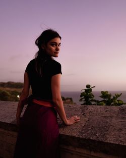 Young woman standing against sky during sunset