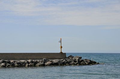 Lighthouse on groyne by sea against sky