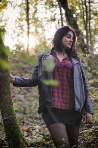 Young woman standing by tree in forest