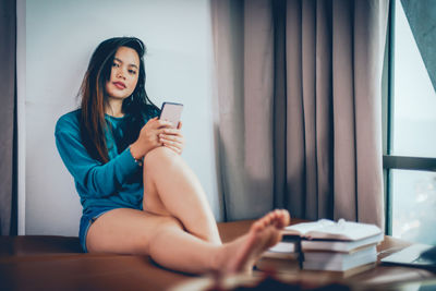 Young woman using mobile phone while sitting on table