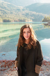 Smiling woman in autumn coat stands on the coast of alps mountain lake eibsee in germany.