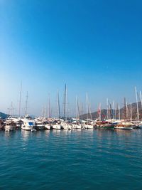 Sailboats moored in harbor against clear blue sky