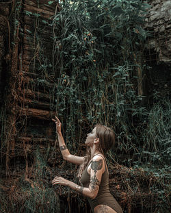 Side view of woman sitting on land in forest