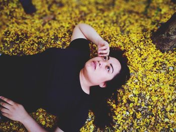 High angle view of young woman looking away while lying on autumn field at park