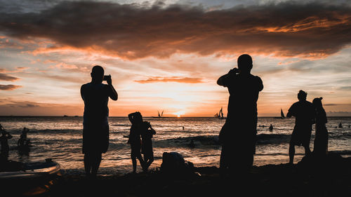 Silhouette people standing at beach during sunset