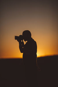 Side view of silhouette photographer against sky during sunset