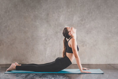 Side view of young woman doing cobra pose on exercise mat
