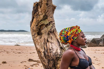 Ghanaian african woman with colorful headdress sitting at a broken palm tree stump