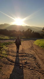 Rear view of man standing on field against sky during sunset