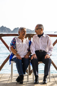 Full length of couple sitting on chair against lake