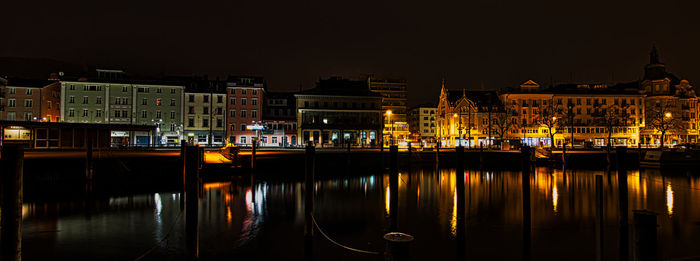 Illuminated buildings by river against sky in city at night