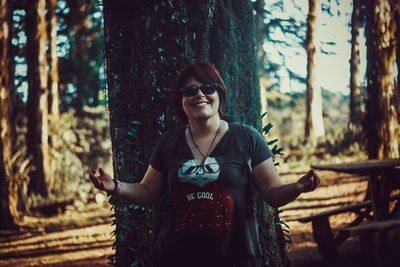 Portrait of young woman standing by tree trunk