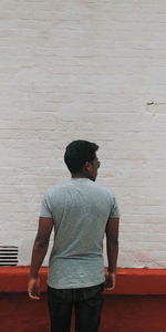 Rear view of young man looking away against wall