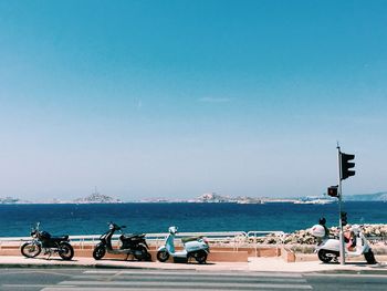 Motor scooters parked on sidewalk against blue sky