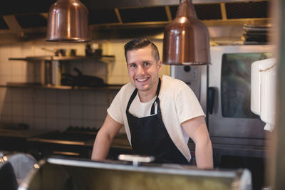 Portrait of smiling young waiter wearing apron in restaurant