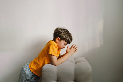 A boy in an orange t-shirt prays at home. concept for faith