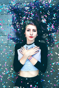 Directly above portrait of beautiful young woman with colorful confetti lying on footpath