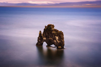 Rock formation in sea against sky during sunset