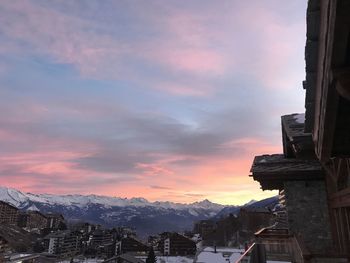 Snow covered buildings against sky during sunset