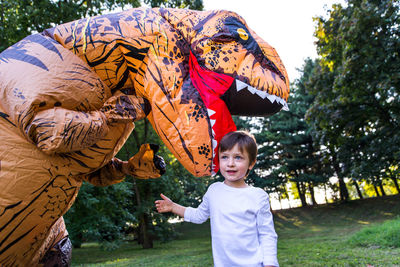 Boy playing with person wearing dinosaur costume in park