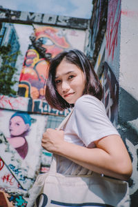 Portrait of smiling young woman standing against graffiti