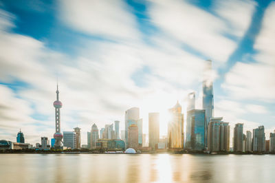 View of skyscrapers by river against cloudy sky