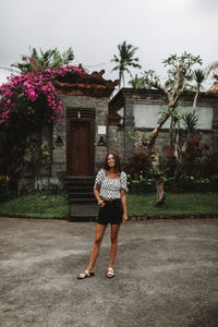 Full length portrait of young woman standing against building