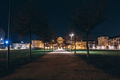 Illuminated street amidst buildings against sky at night