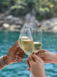 Cropped hands toasting wine at swimming pool