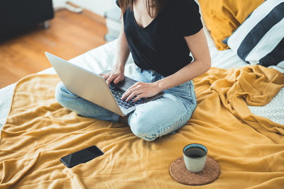 High angle view of woman using laptop on bed at home  female relaxing and drinking cup of hot coffee