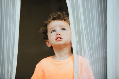 Portrait of boy looking through window at home
